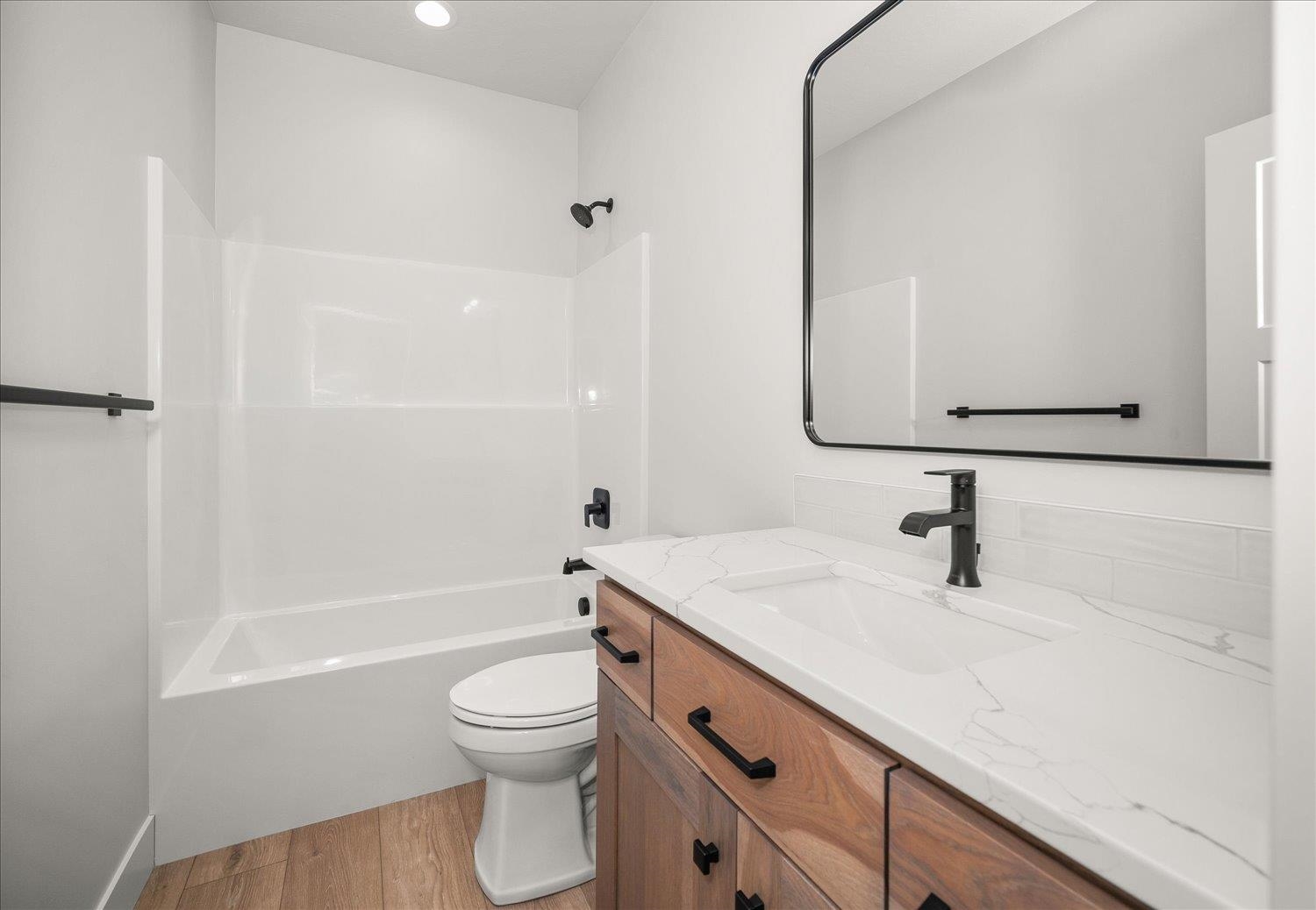 Modern bathroom with a white tub and shower, wood vanity, veined countertop, and black fixtures.