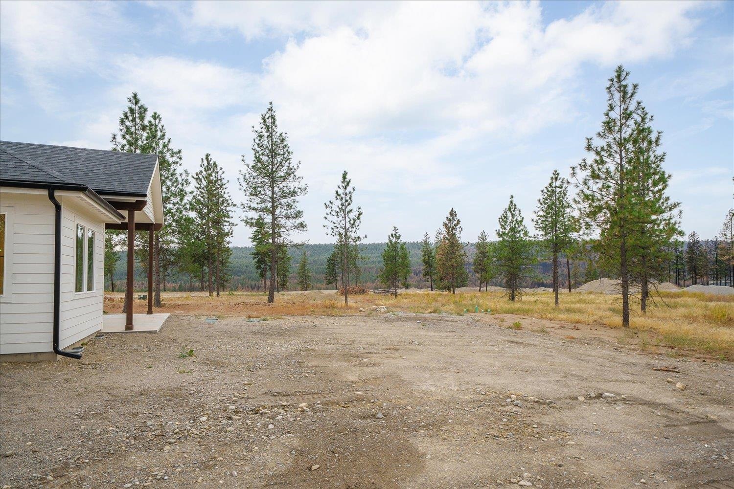 Home beside a broad gravel lot, with pine trees and wooded hills in the background.