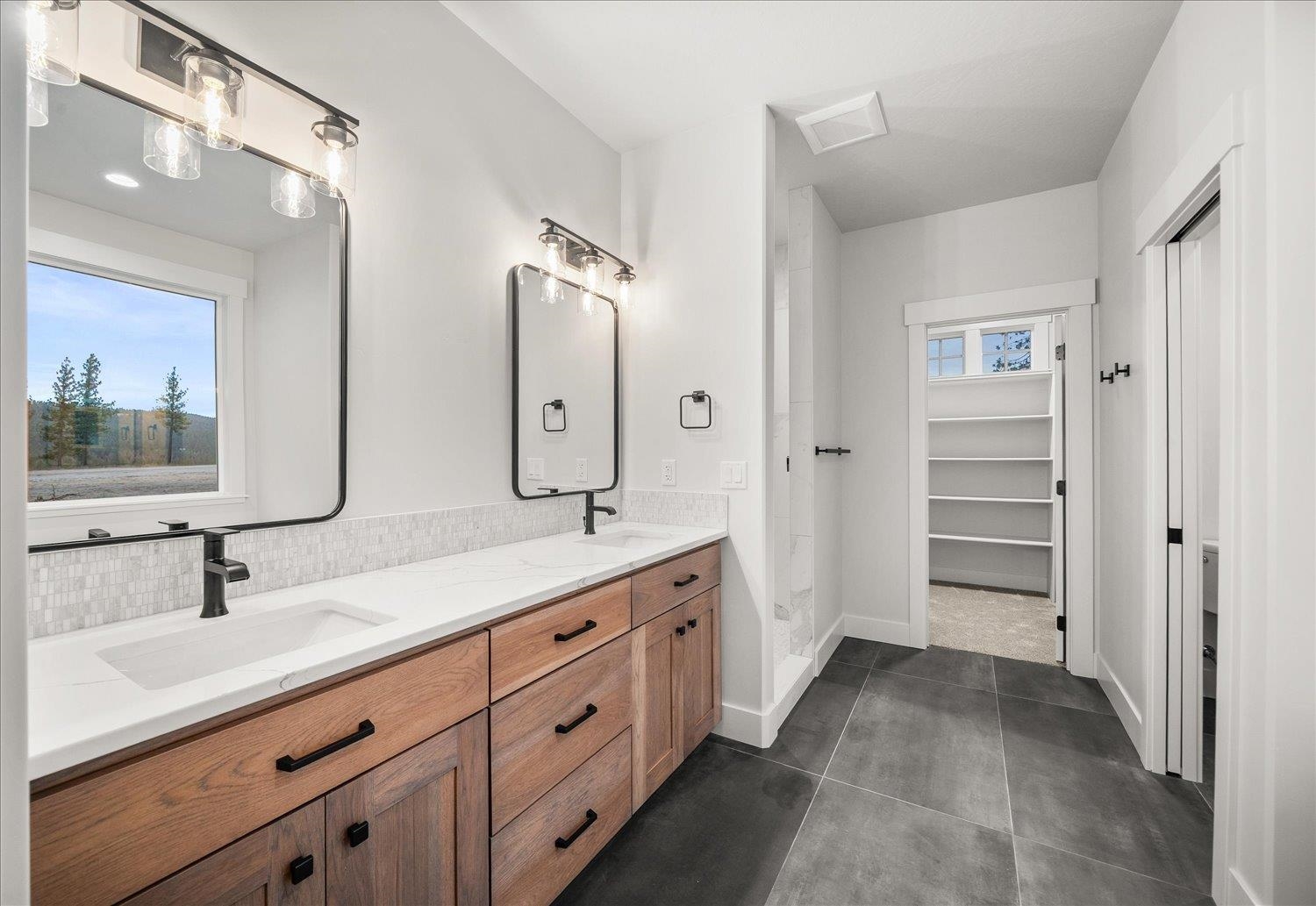 Bathroom with a wood double vanity, white counters, black faucets, and a tiled shower area.
