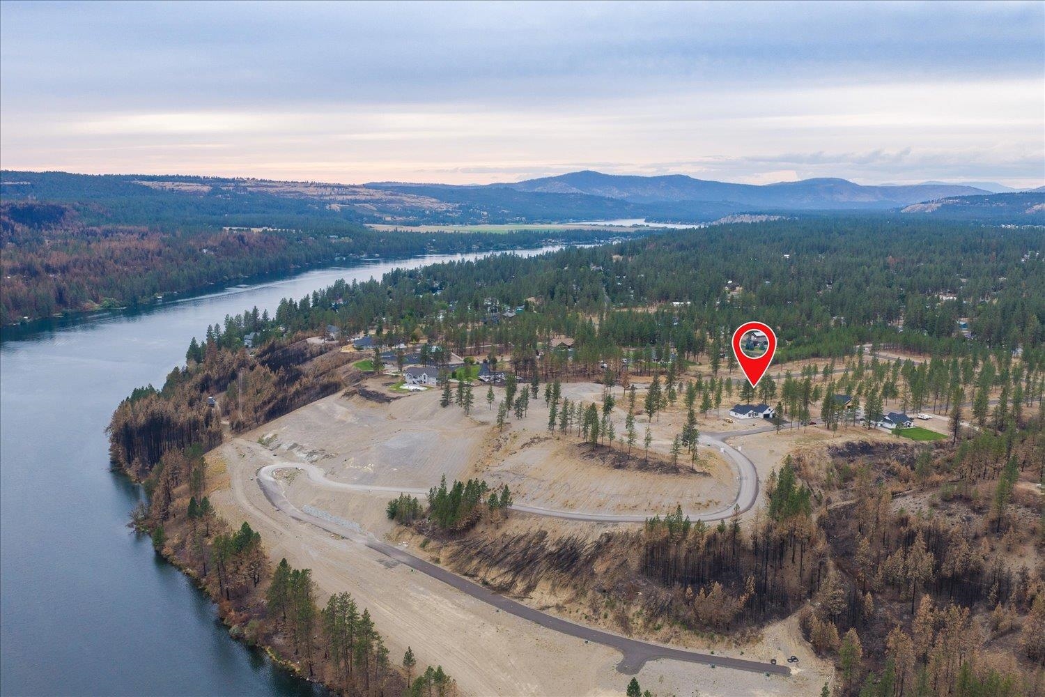 Aerial view of the homesite amid wooded lots beside a lake, with distant mountains.