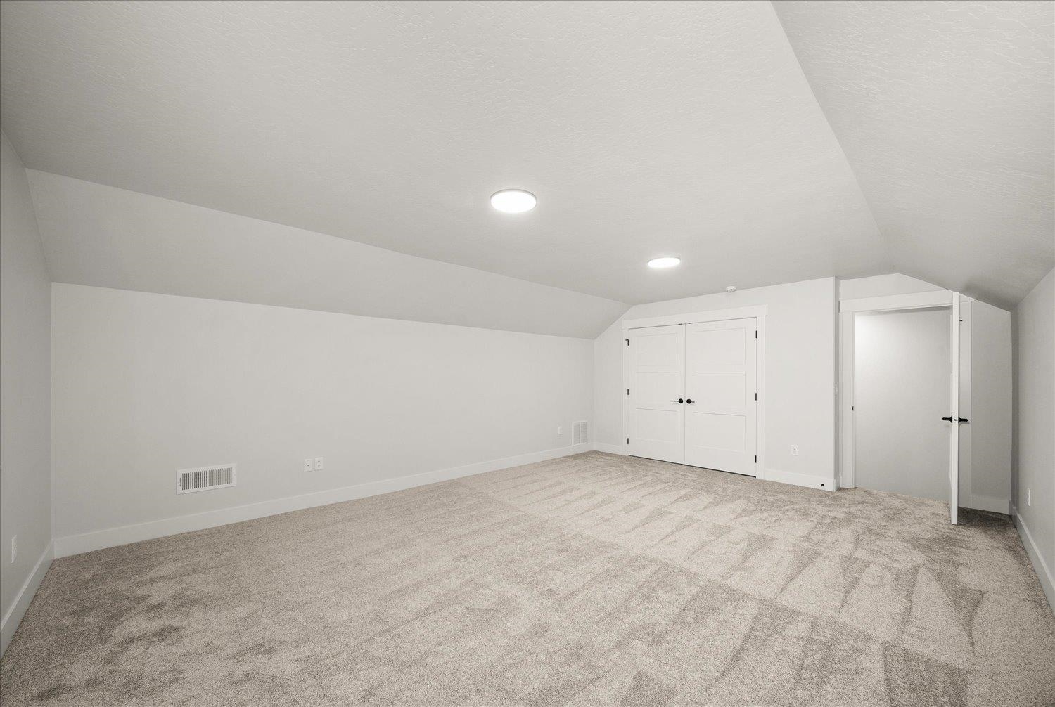 Empty carpeted room with a sloped ceiling, double closet doors, and an open doorway.
