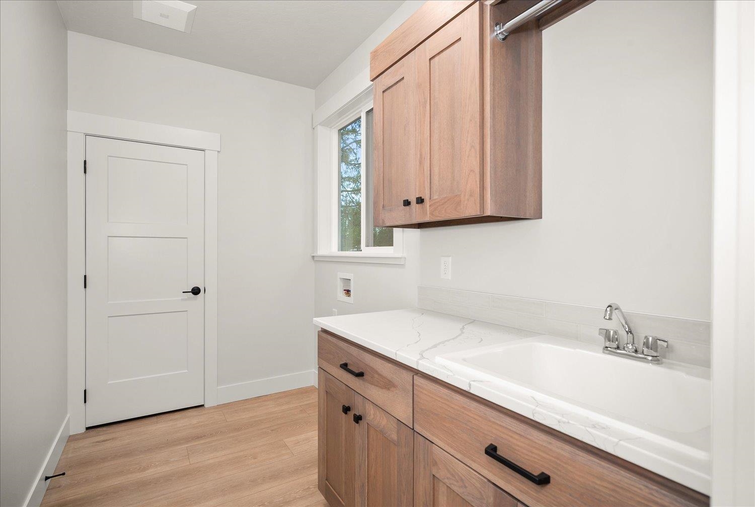 Bathroom with a white sink and countertop, natural wood cabinetry, and a window beside the door.