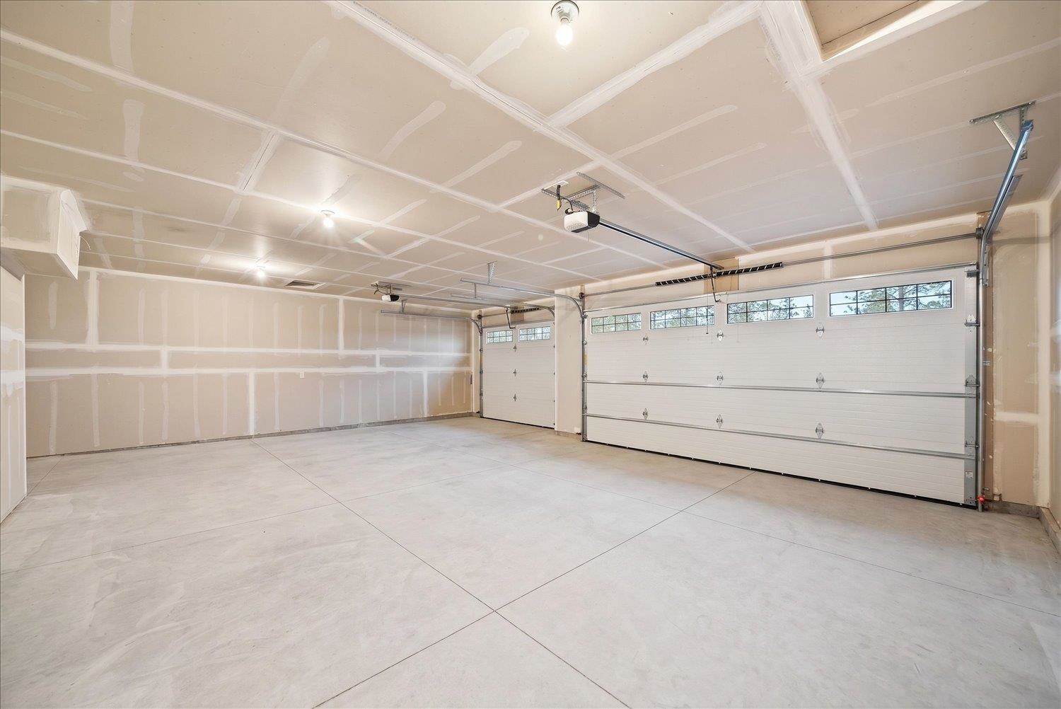 Empty garage with two overhead doors, upper windows, and unfinished drywall.