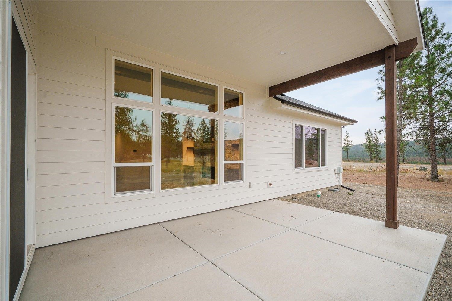 Covered concrete patio along a light-sided home, with large windows and dark timber supports.
