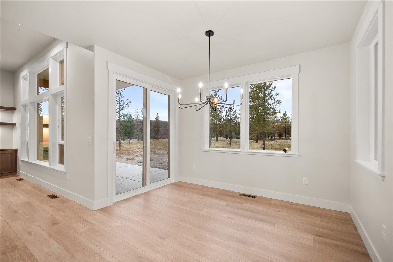 Empty dining area with a modern chandelier, large windows, and sliding doors to a patio.