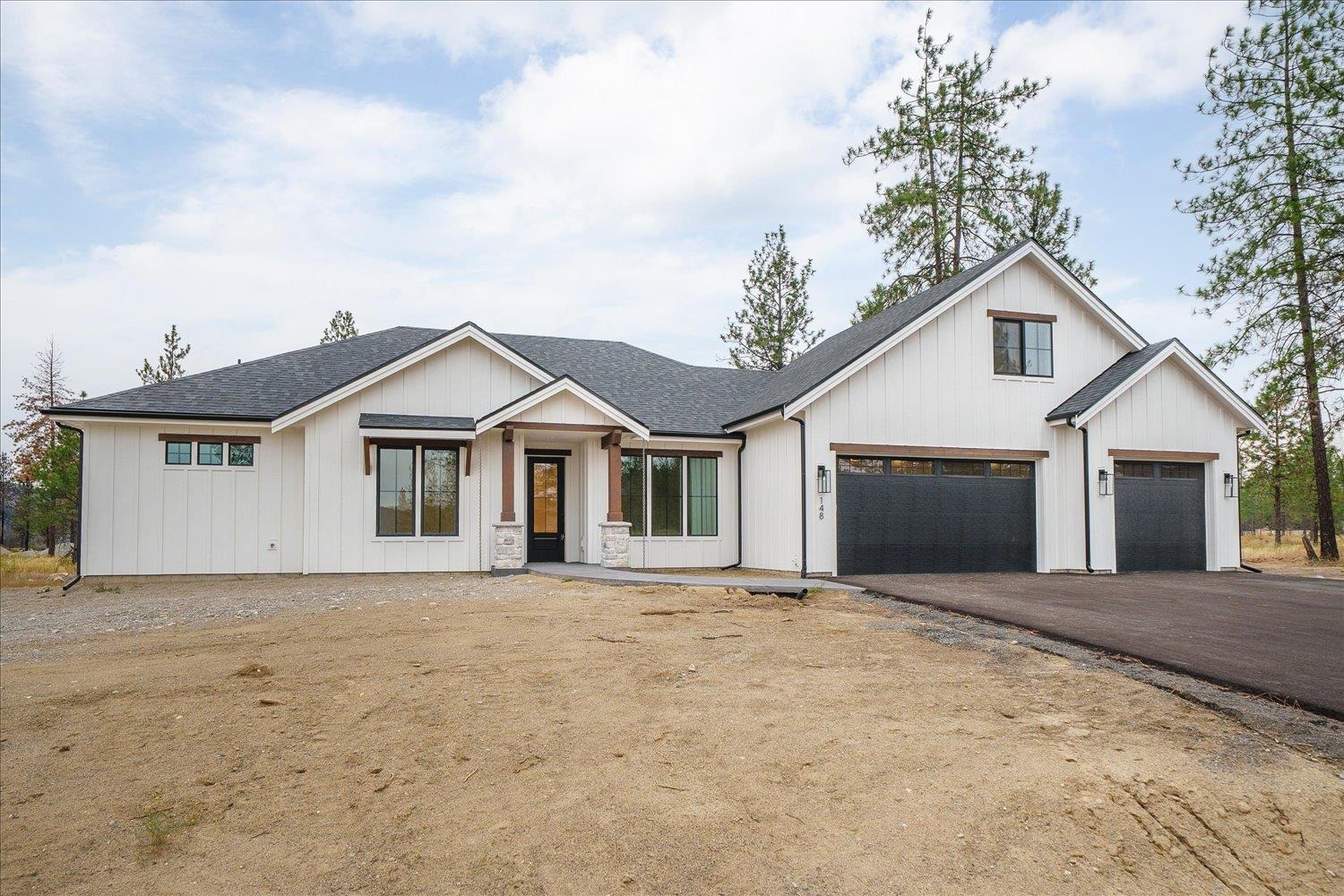 White home with two black garage doors, a covered entry, and a broad unfinished front yard.