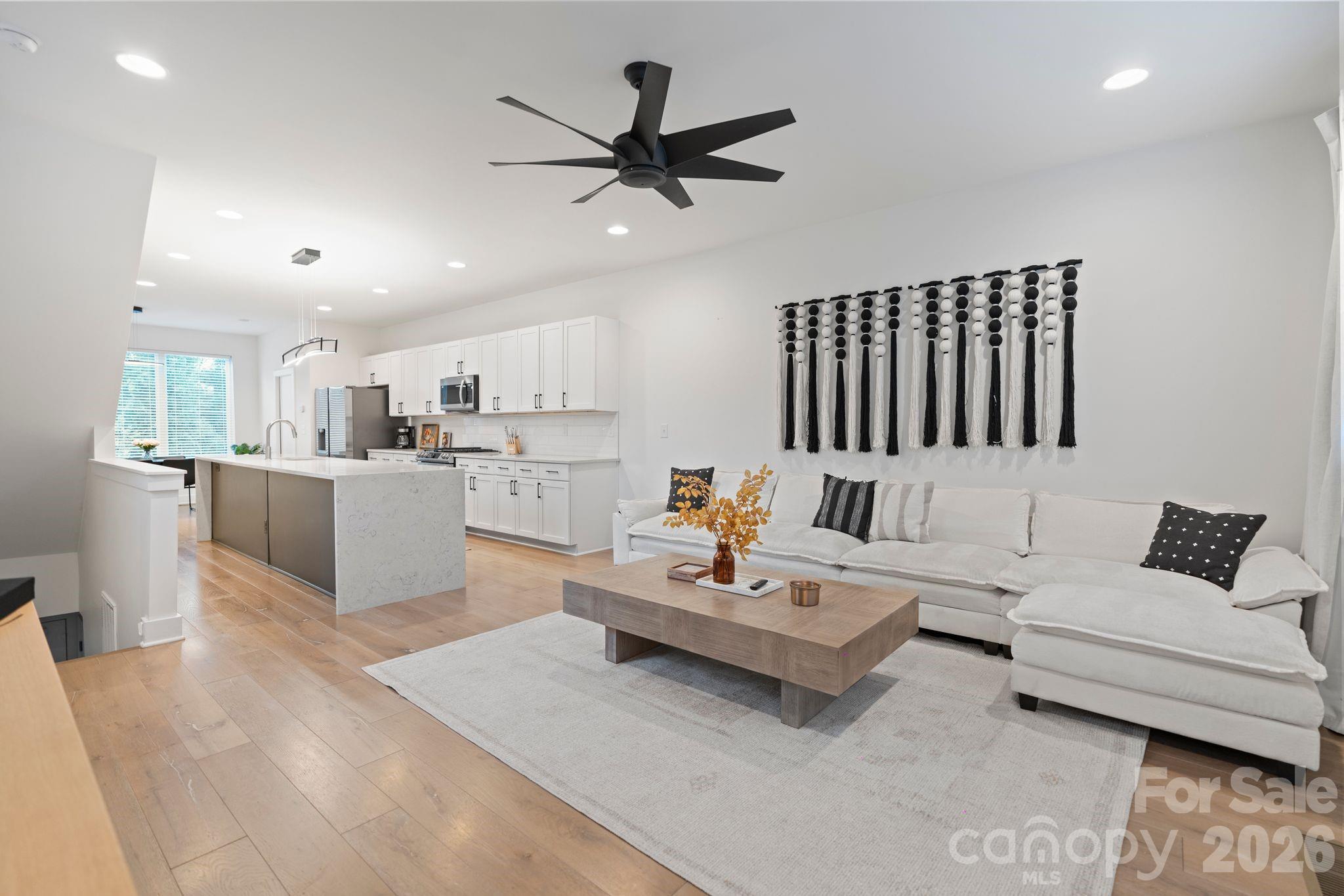 Open-plan living room and kitchen with a marble-look island, white sectional sofa, and black ceiling fan.
