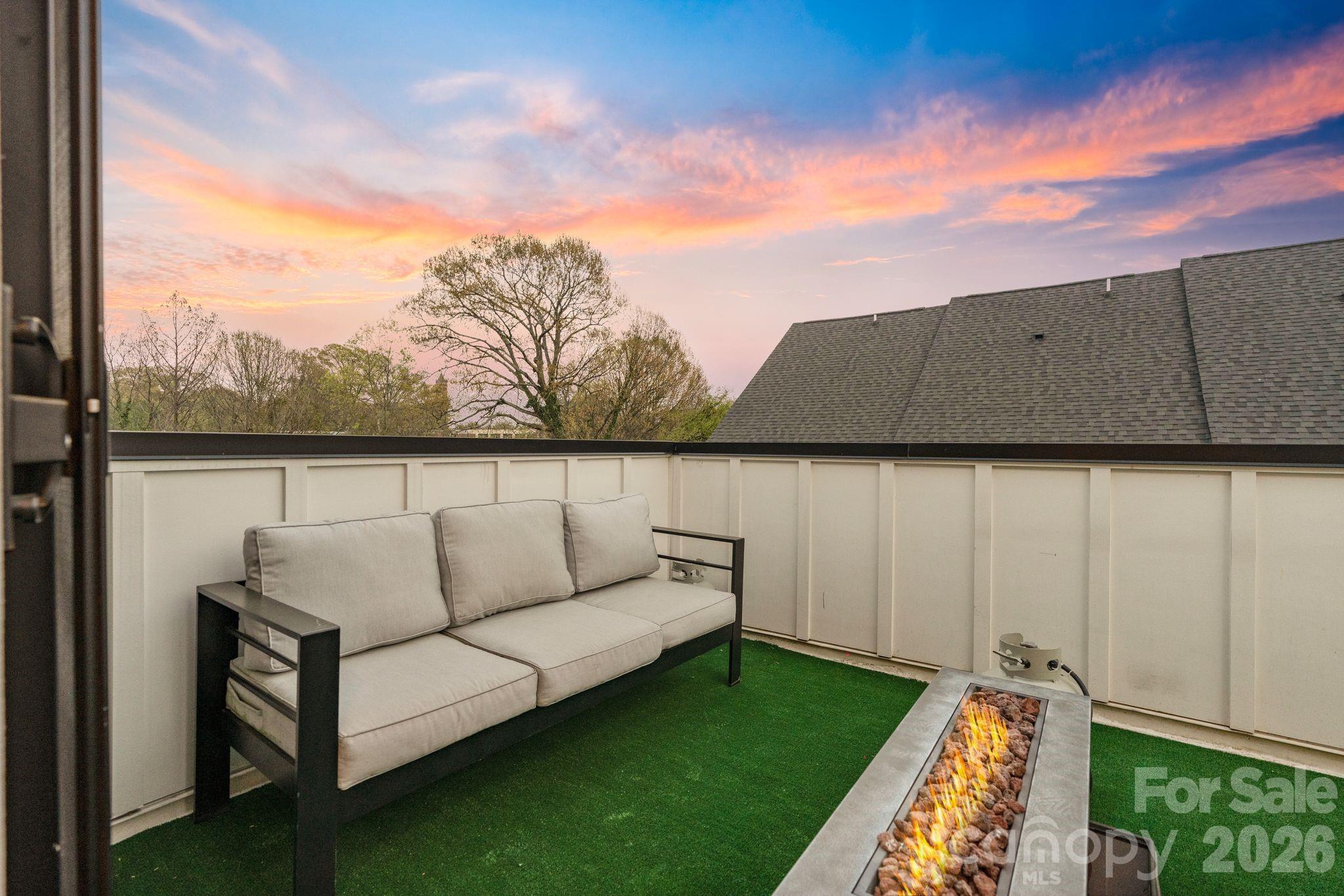 Rooftop terrace with a cushioned sofa and lit fire pit beneath a colorful sunset sky.
