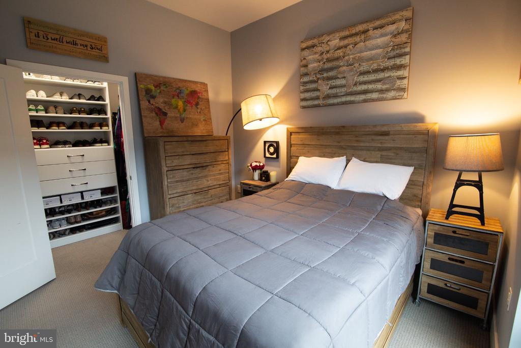 Furnished bedroom with a gray quilted bed, rustic wood furniture, and an open shoe closet.