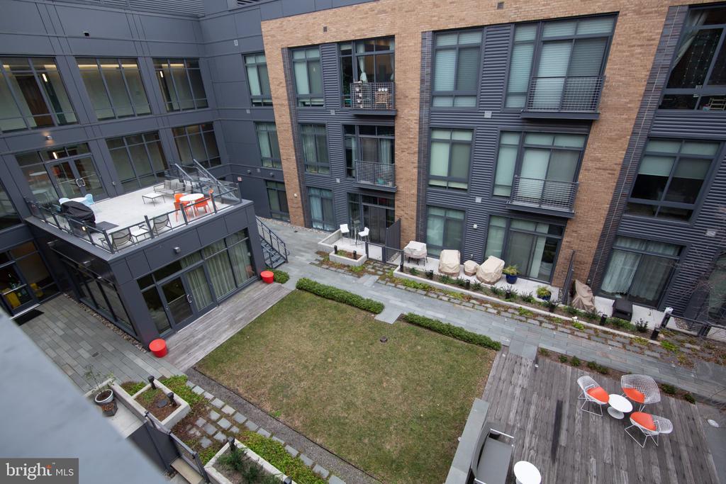 Condominium courtyard with a central lawn, paved paths, and outdoor seating among brick-and-metal facades.