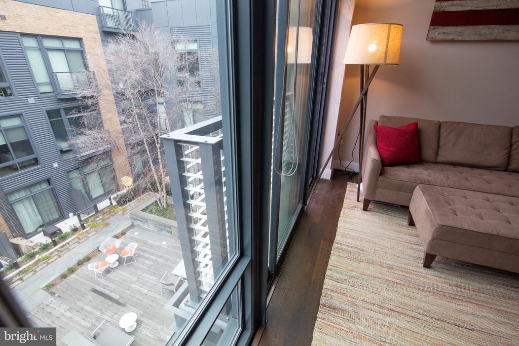 Living room with a taupe sectional beside floor-to-ceiling windows overlooking a courtyard patio.