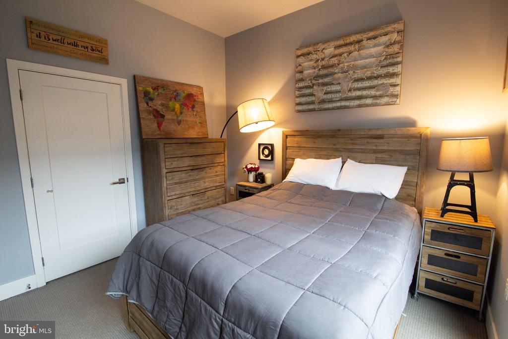 Bedroom with a gray quilted bed, rustic wood headboard, matching dresser, and warm bedside lamps.