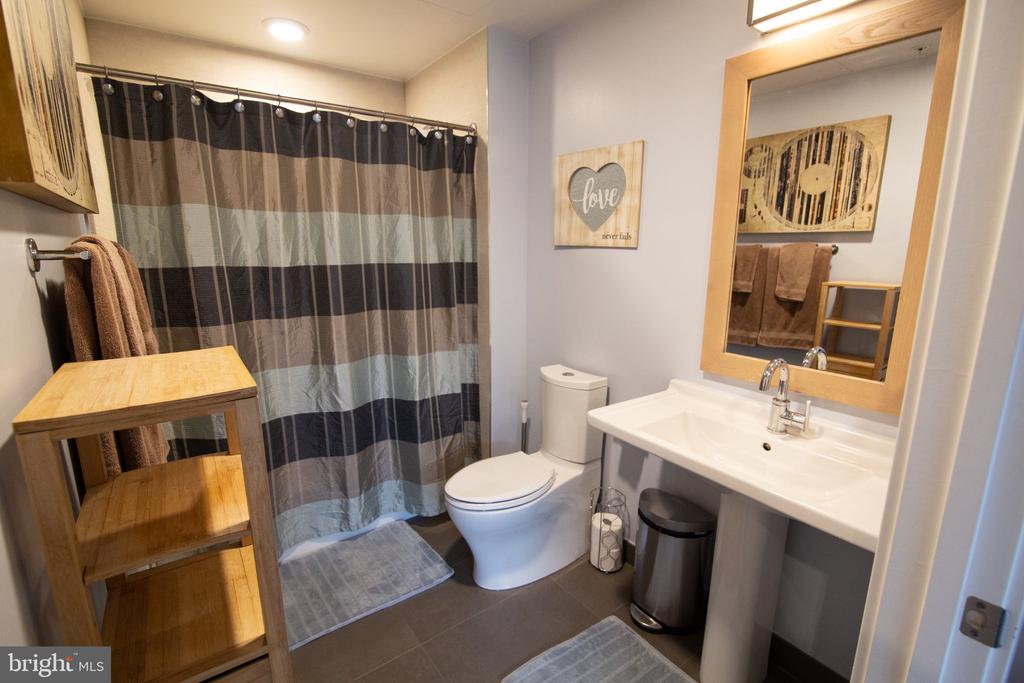 Furnished bathroom with a white vanity, toilet, striped shower curtain, and wooden shelving.