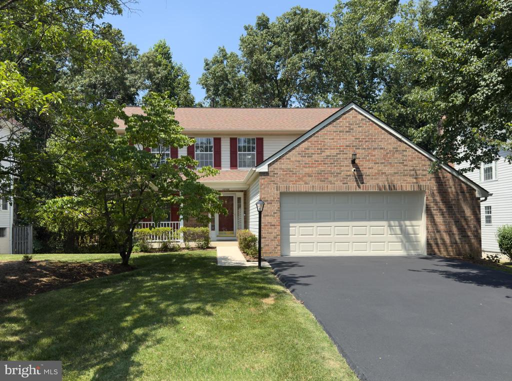 Two-story house with a brick garage, red shutters, and a tree-shaded front lawn.