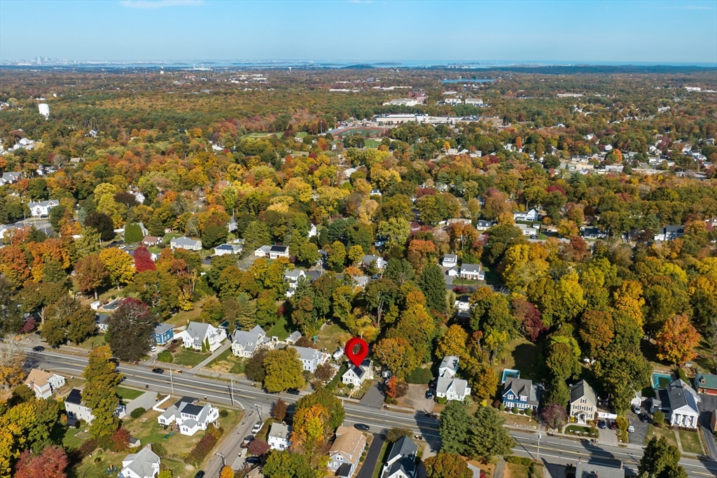 Aerial view of an autumn neighborhood, with a red pin marking a house beside the main road.