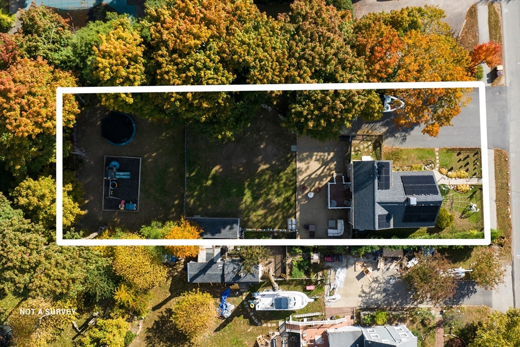 Aerial view of the outlined property, with a tree-shaded yard and solar panels on the house.