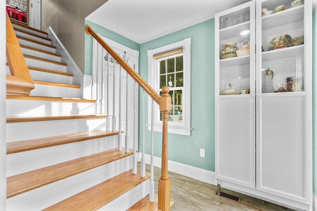 Staircase with natural wood treads and handrail beside a glass-front display cabinet.