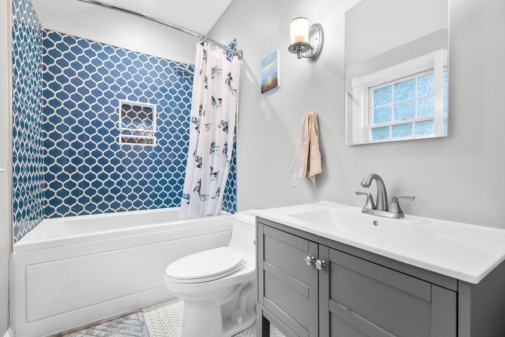 Bathroom with blue patterned tile around the tub and a gray vanity.