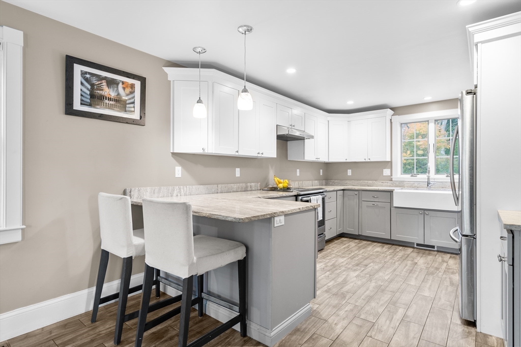 Kitchen with white cabinets, gray island, stone counters, farmhouse sink, and stainless steel appliances.