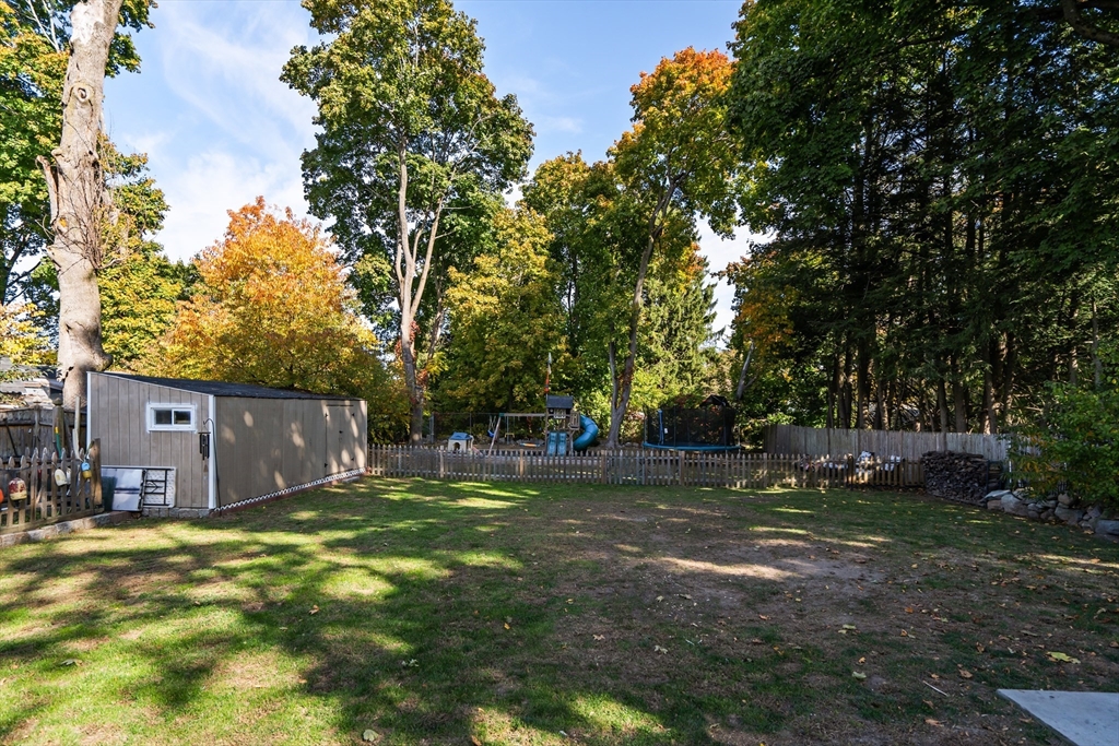 Fenced backyard with a lawn, storage shed, playset, and mature trees.