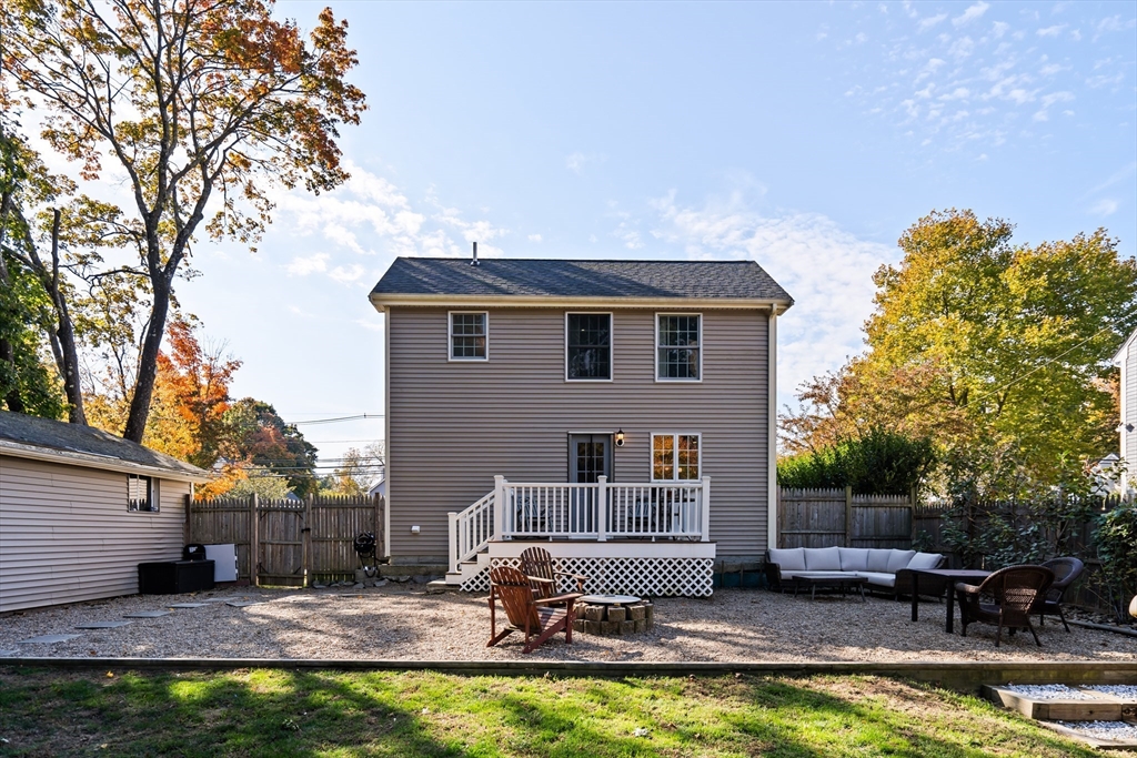 House rear with raised deck, gravel patio, fire pit, and outdoor seating in a fenced yard.