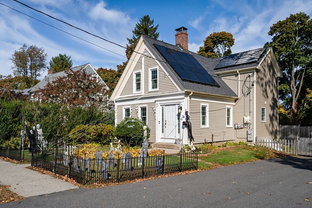 Beige two-story home with rooftop solar panels and Halloween decorations in its fenced front yard.
