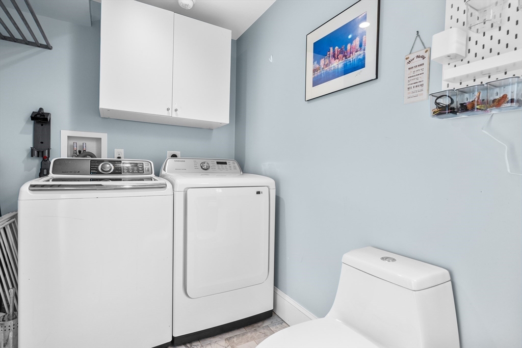 Laundry room with a white washer and dryer, wall cabinets, and a toilet.
