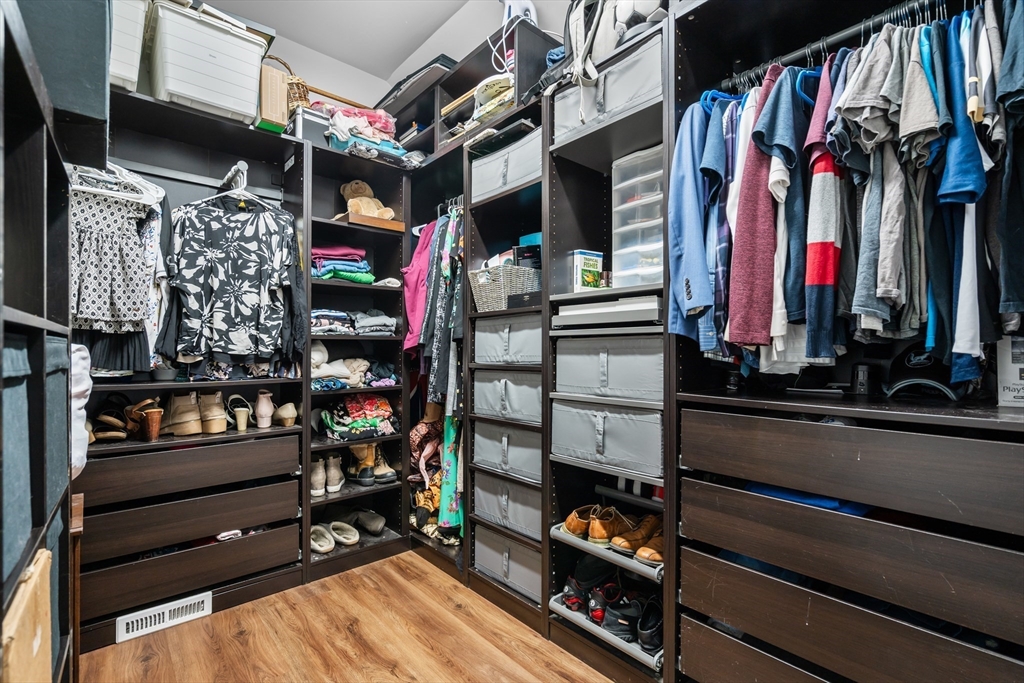 Walk-in closet with extensive dark built-in storage, hanging clothes, and shoes.