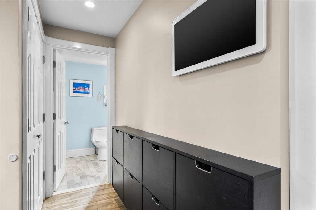 Hallway with dark storage cabinets and a wall-mounted television, opening to a blue-walled bathroom.