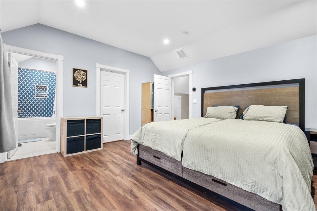 Bedroom with a large bed, wood-look flooring, and an open doorway to a bathroom.