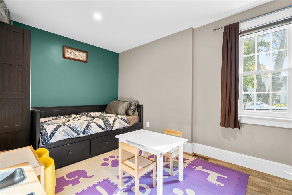Bedroom with a dark built-in daybed, teal accent wall, colorful play mat, and large window.