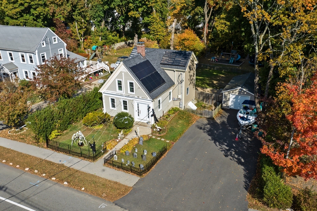Aerial view of a two-story home with rooftop solar panels, fenced yard, and detached garage.