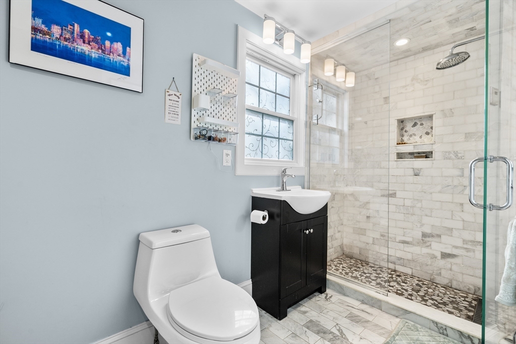 Bathroom with a glass walk-in shower, marble-look tile, pebble floor, and black vanity.