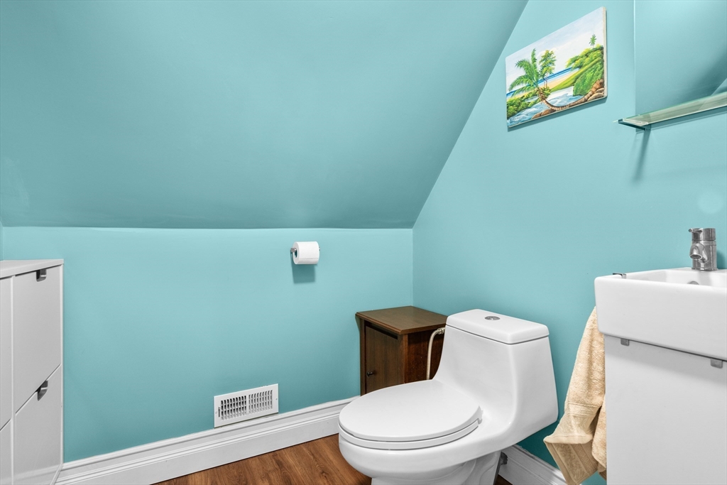 Turquoise bathroom with a sloped ceiling, white toilet and sink, and wood-look flooring.