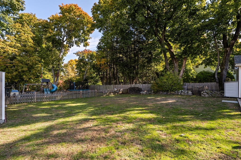 Fenced backyard with mature trees, autumn foliage, and a children’s playset