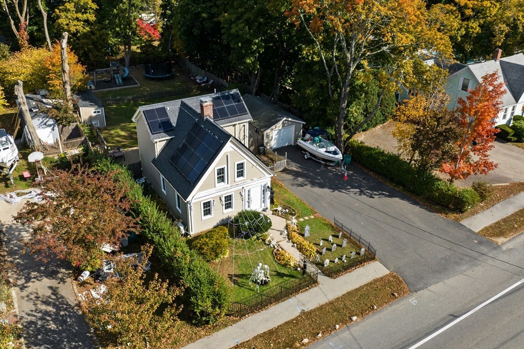 Aerial view of a home with rooftop solar panels, fenced yard, and a boat beside the driveway.