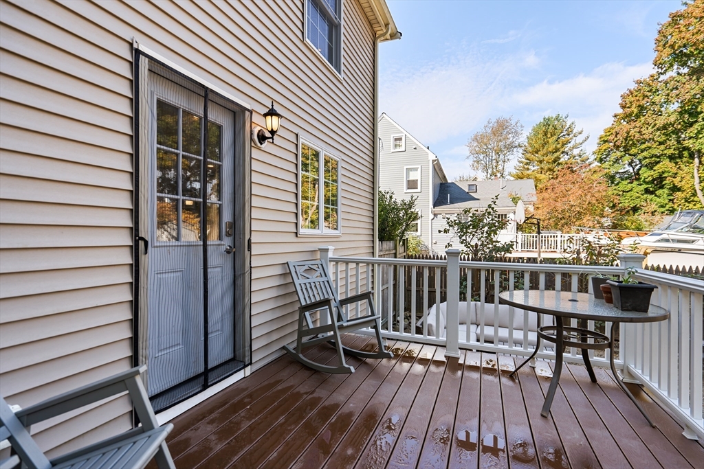 Raised wooden deck with white railings, a screened door, rocking chairs, and outdoor dining furniture.