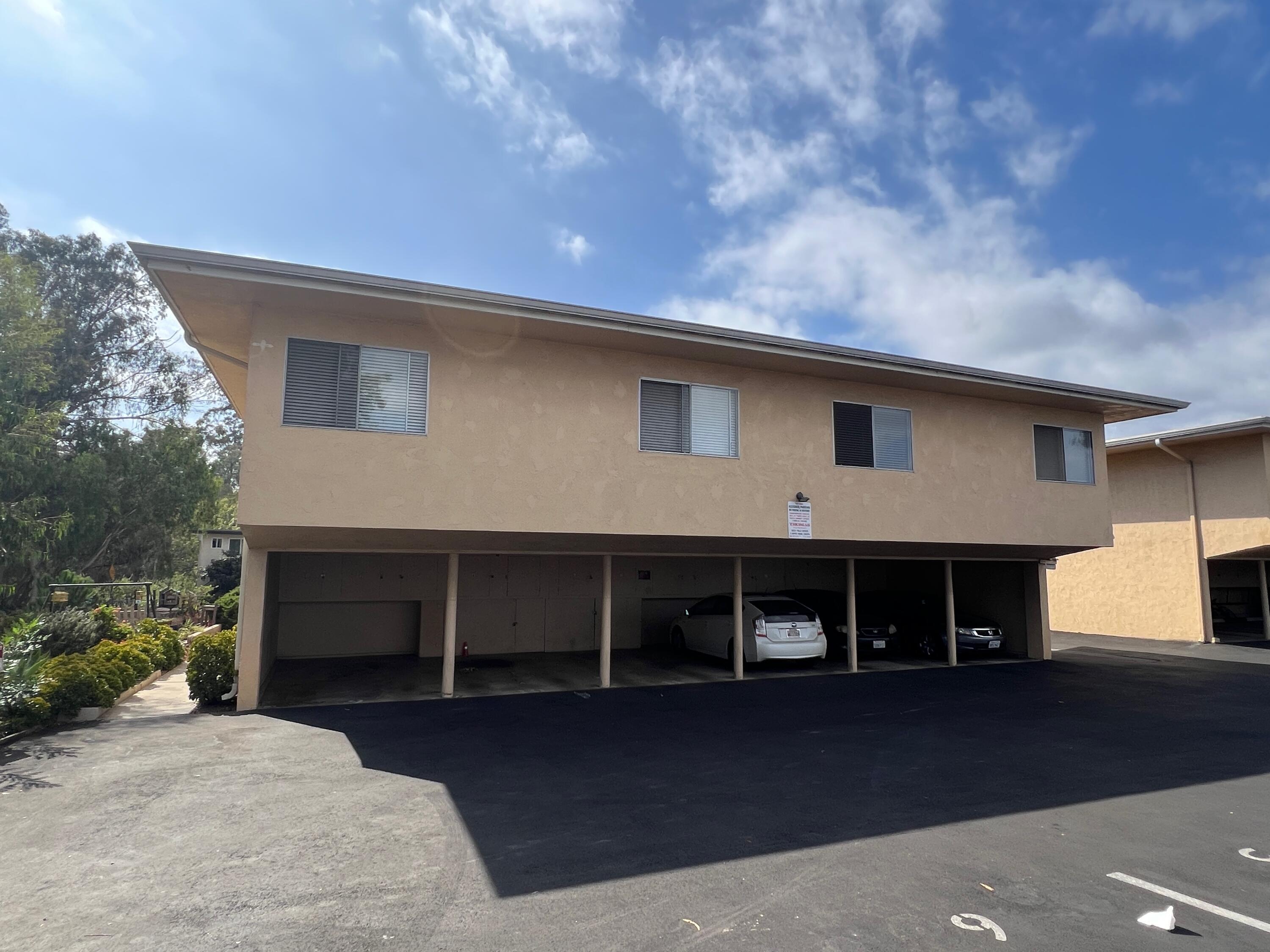 Tan two-story residential building with open carport parking and several cars beneath.
