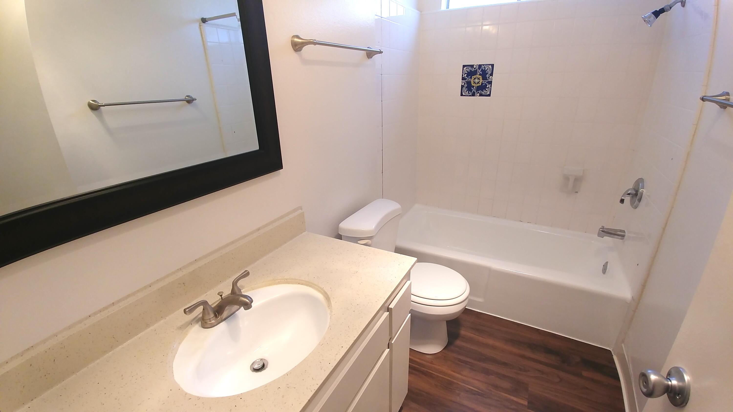 Bathroom with a beige vanity, white tub and toilet, dark flooring, and decorative blue tile accent.