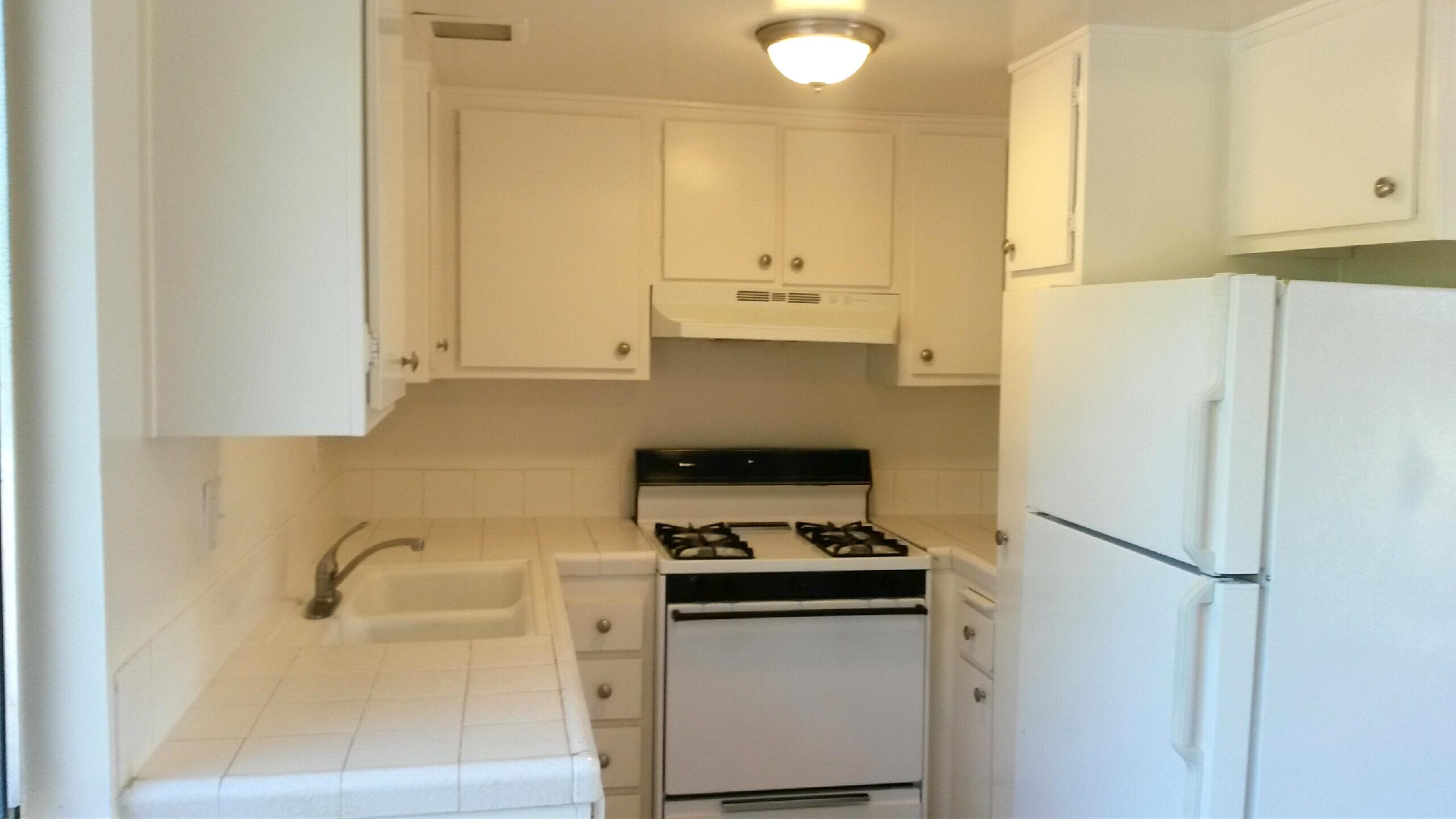 Compact kitchen with white cabinets, tiled counters, a gas range, and refrigerator