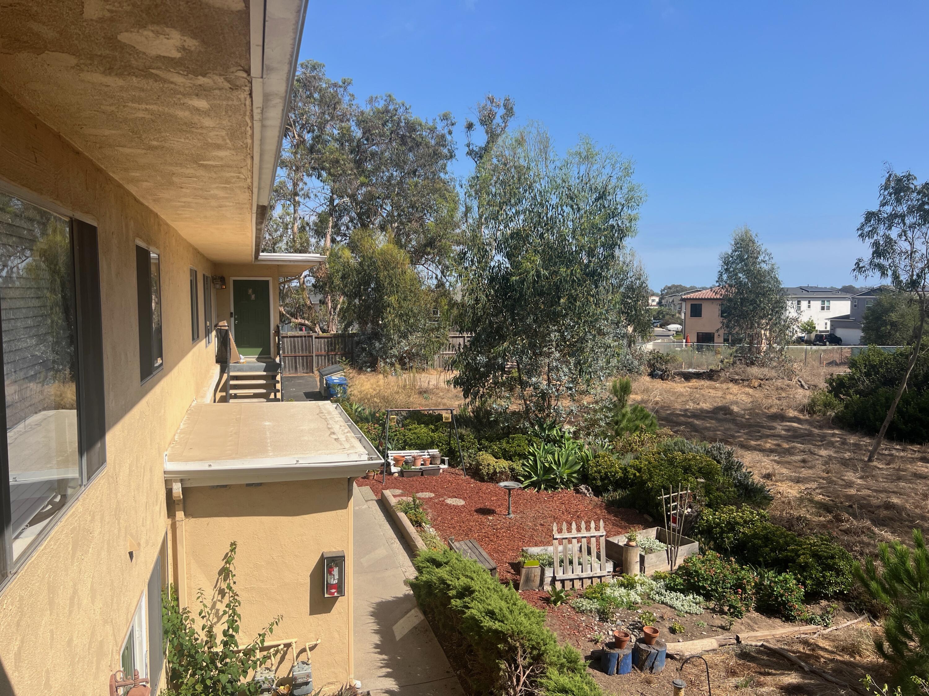 Home’s side patio and garden, with steps to a green entry door beside a dry open yard.