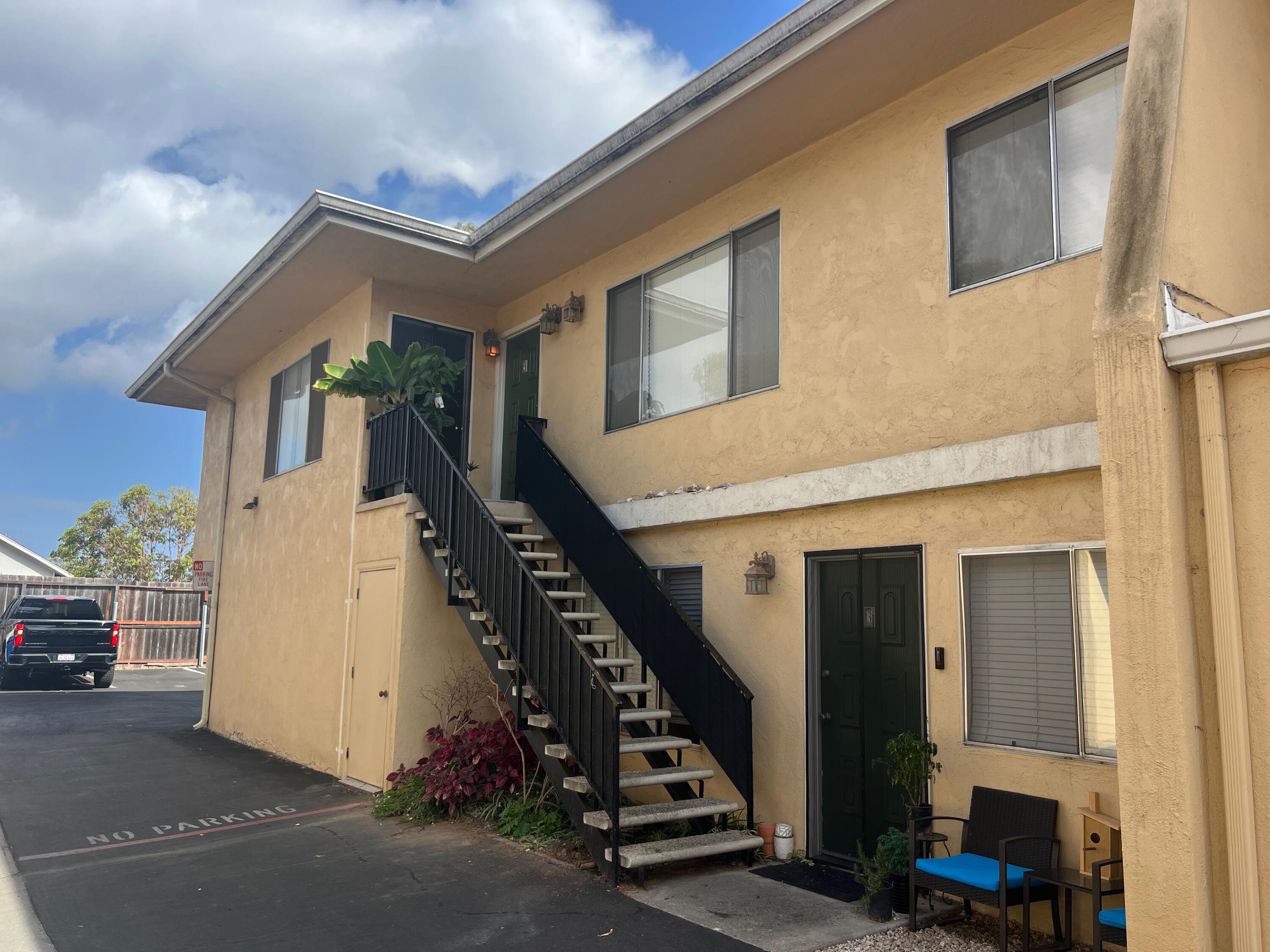 Tan two-story residence with black exterior stairs, green doors, and a no-parking lane.