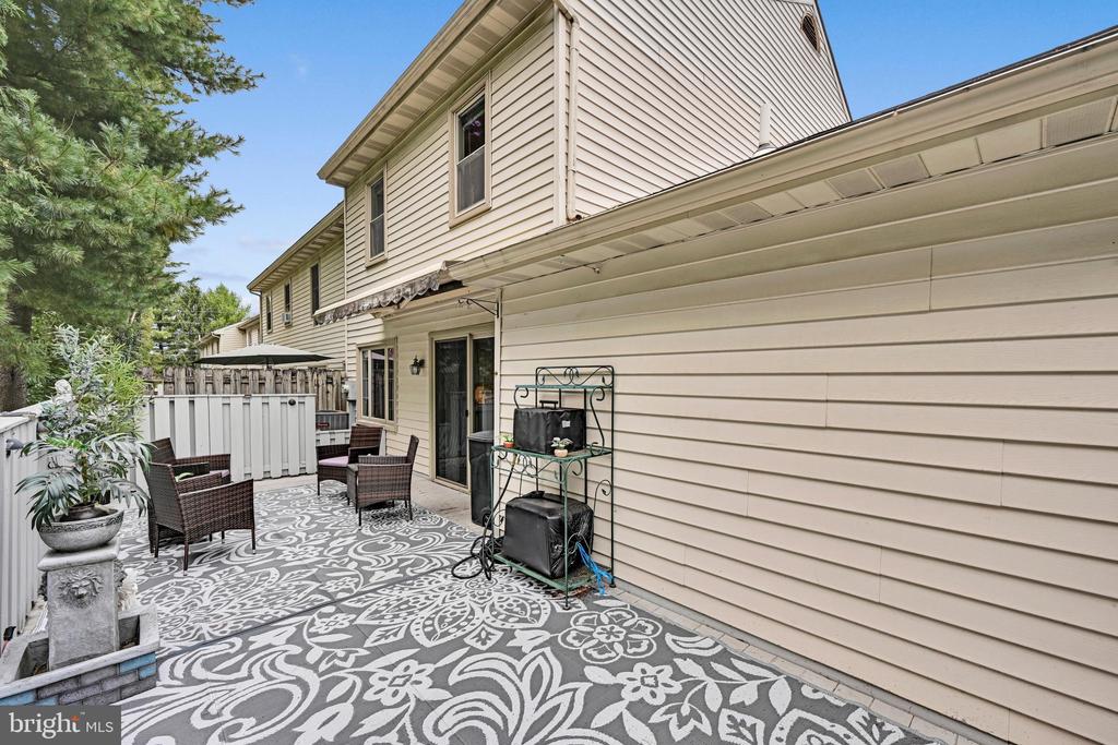 Rear patio with a patterned rug, wicker seating, and a covered area beside the house.