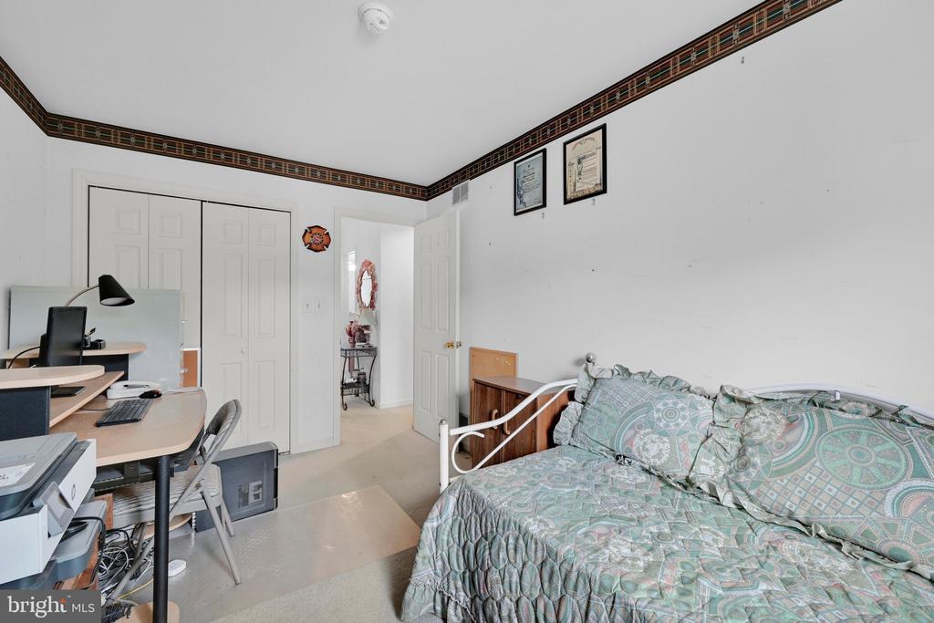 Bedroom with teal patterned bedding and a desk workstation beside white paneled closet doors.
