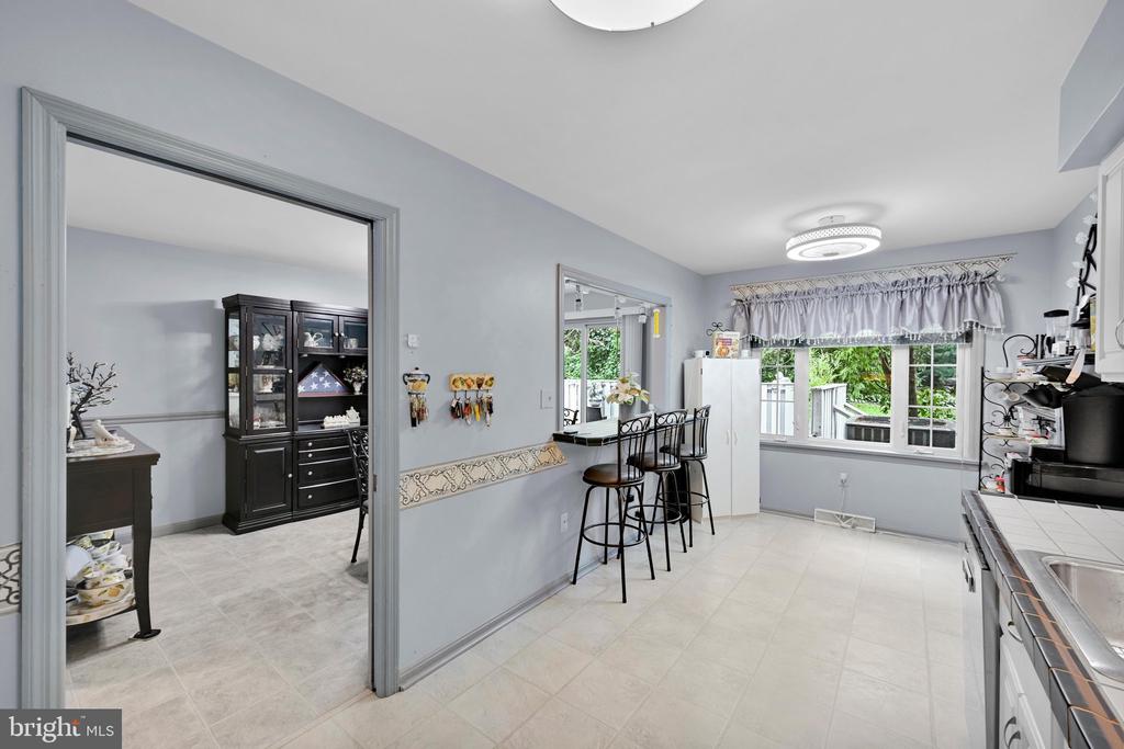 Kitchen with a breakfast bar, pale tile floors, and a large window overlooking greenery.
