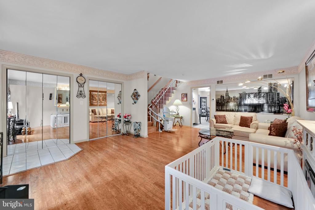 Living room with a cream sectional, wood floors, and a white crib in the foreground.