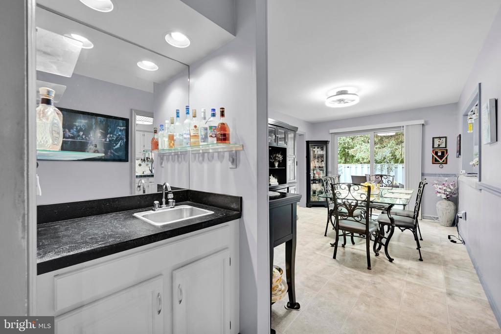Wet bar with black countertop and sink beside a dining area with sliding glass doors.