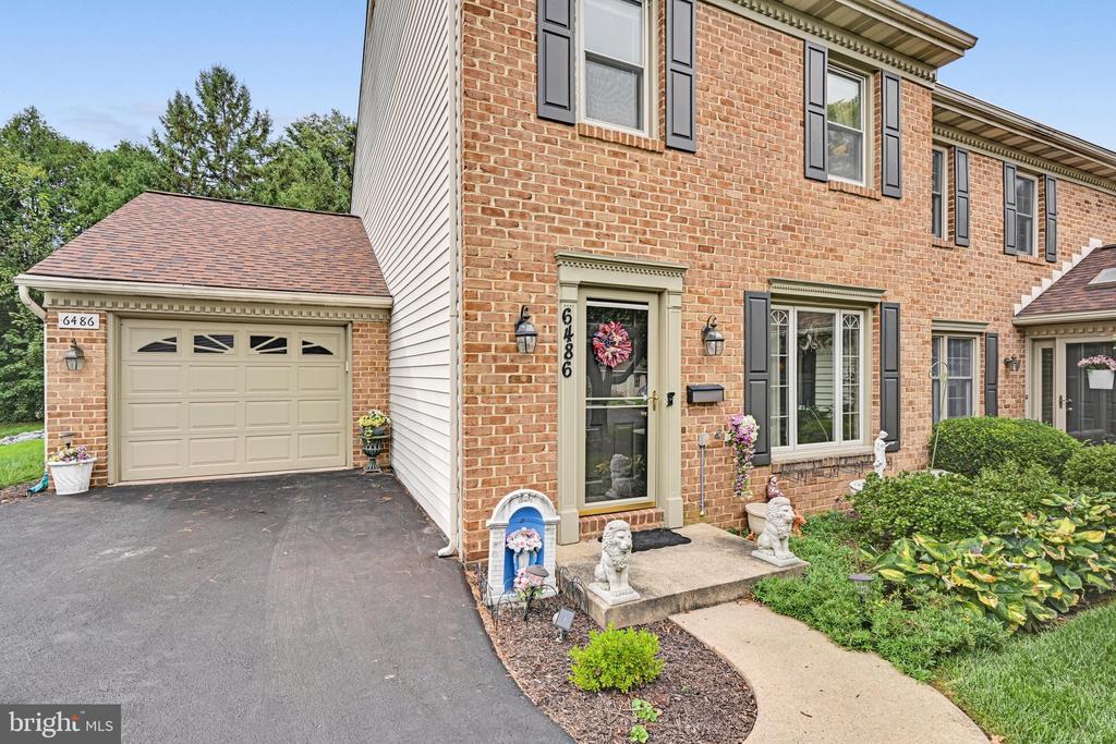 Brick townhouse exterior with attached garage, dark shutters, and landscaped front entry.