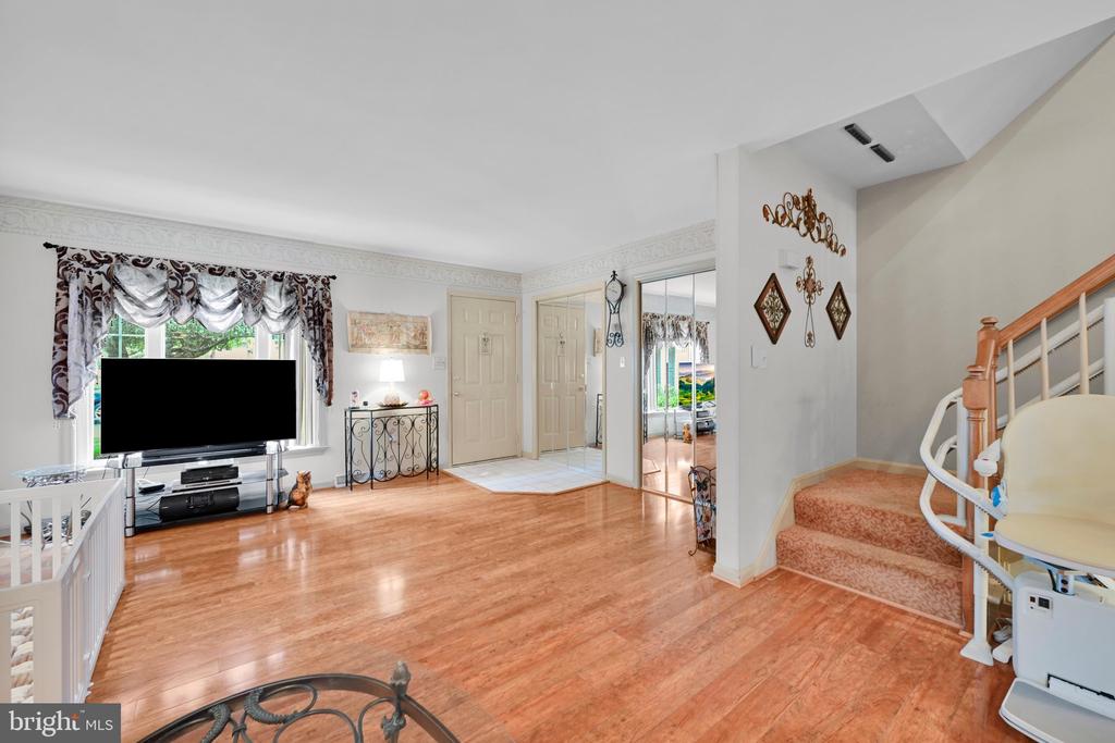 Living room with hardwood floors, a television beside the window, and a carpeted staircase with a stair lift.