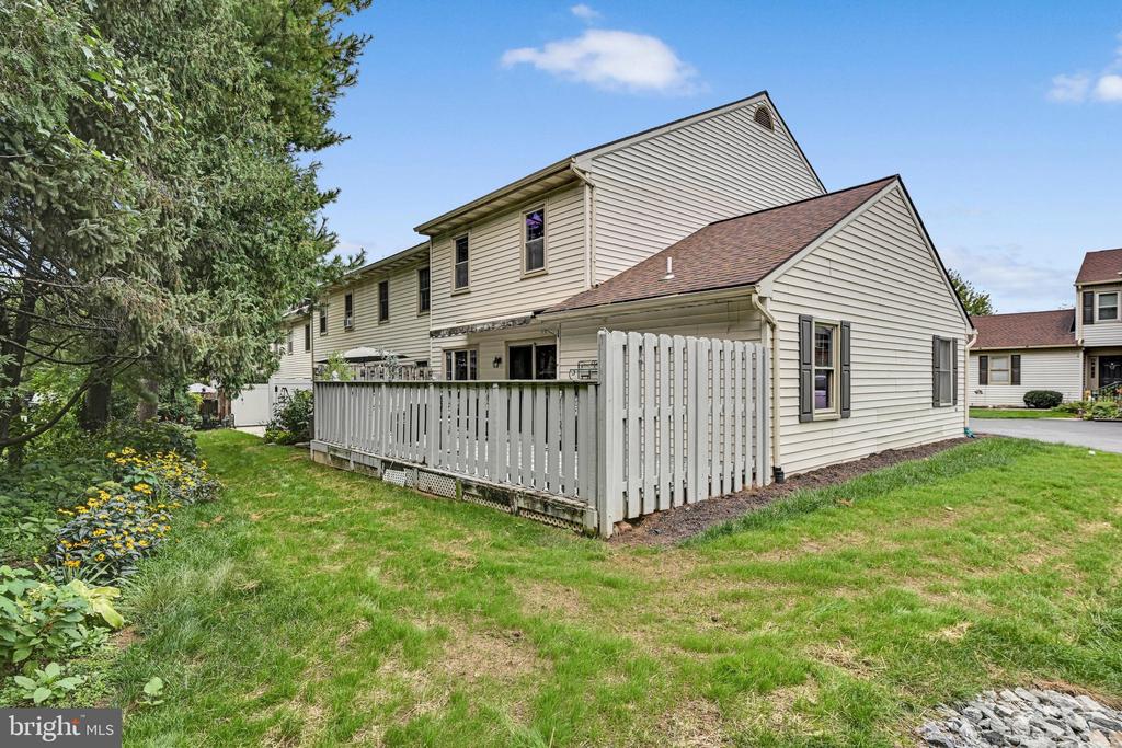 Townhouse rear exterior with a fenced patio, green lawn, and mature trees.